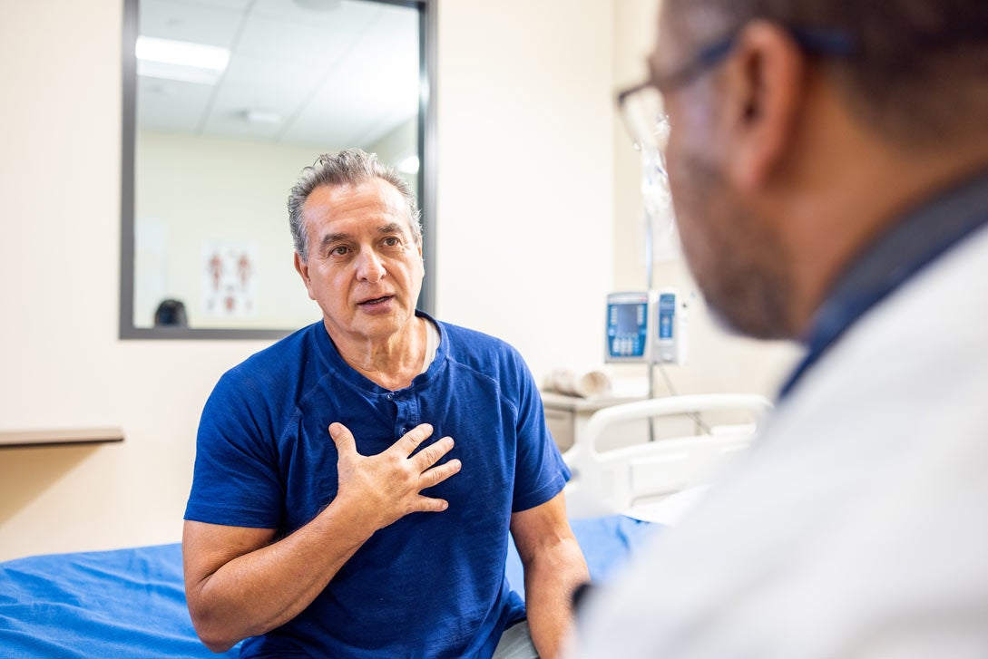 older man gesturing with hand on chest, talking to doctor