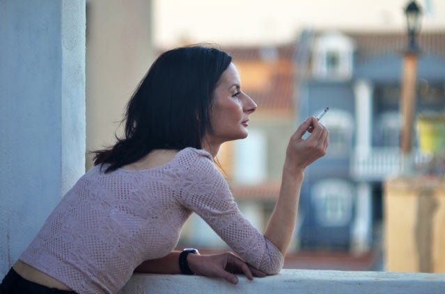 A woman smokes a cigarette on a balcony